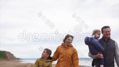 一个幸福的家庭，孩子们穿着温暖的衣服，在一个刮风的日子里在海边漫步